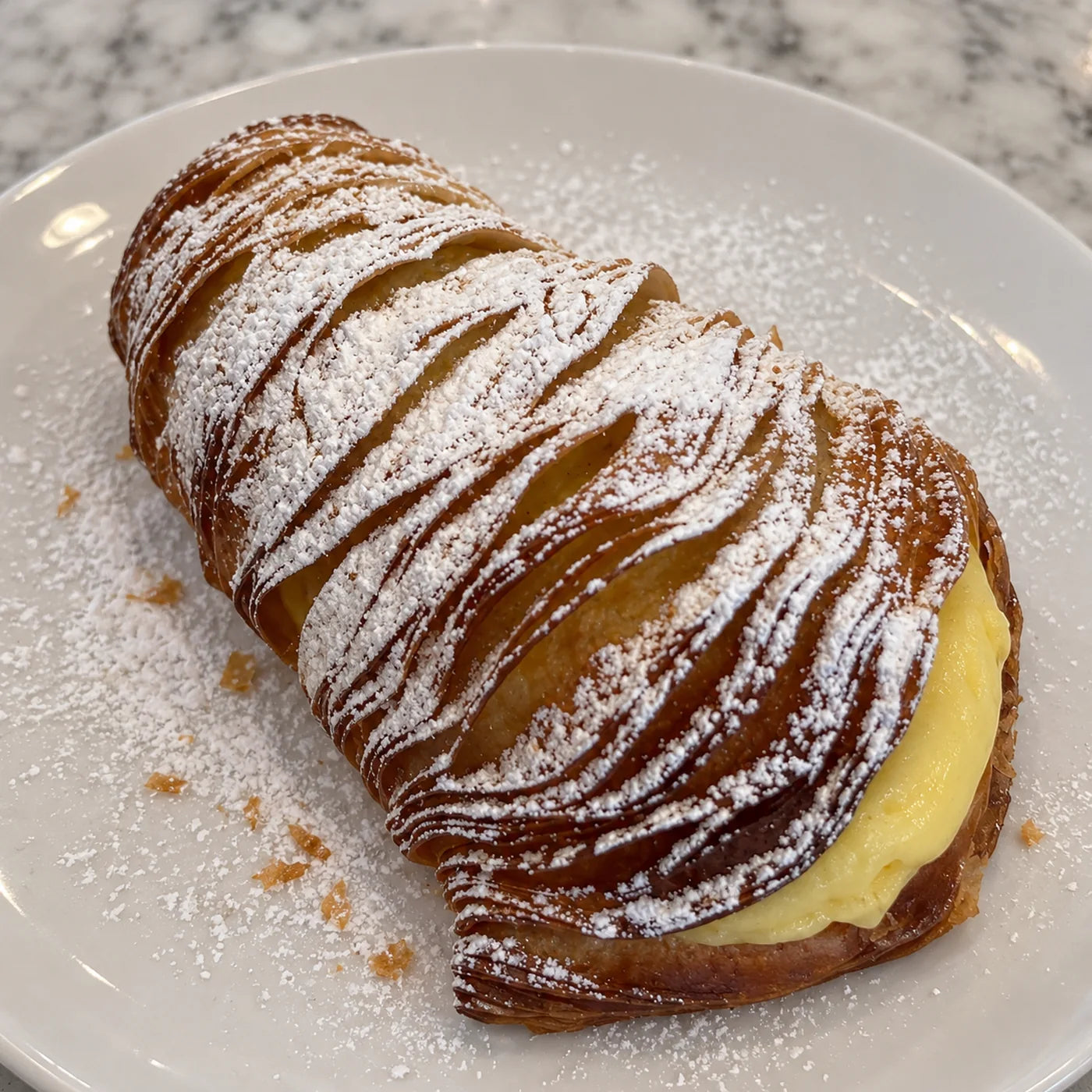 Italian lobster tail pastry, a sfogliatella riccia of crisp ribboned layers dusted with powdered sugar and filled with vanilla cream